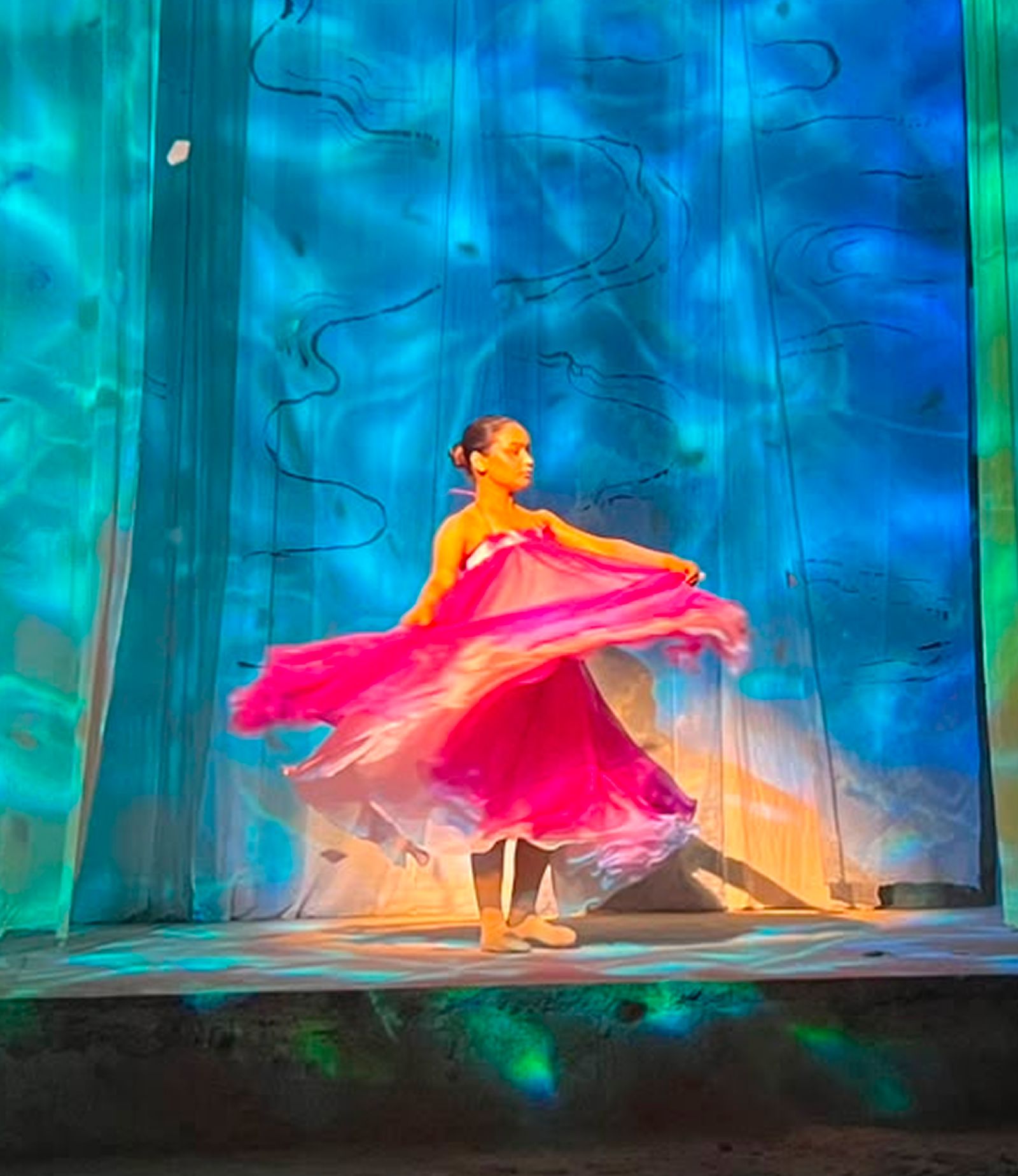Dancer in a flowing pink dress on a stage lit with blue and green light