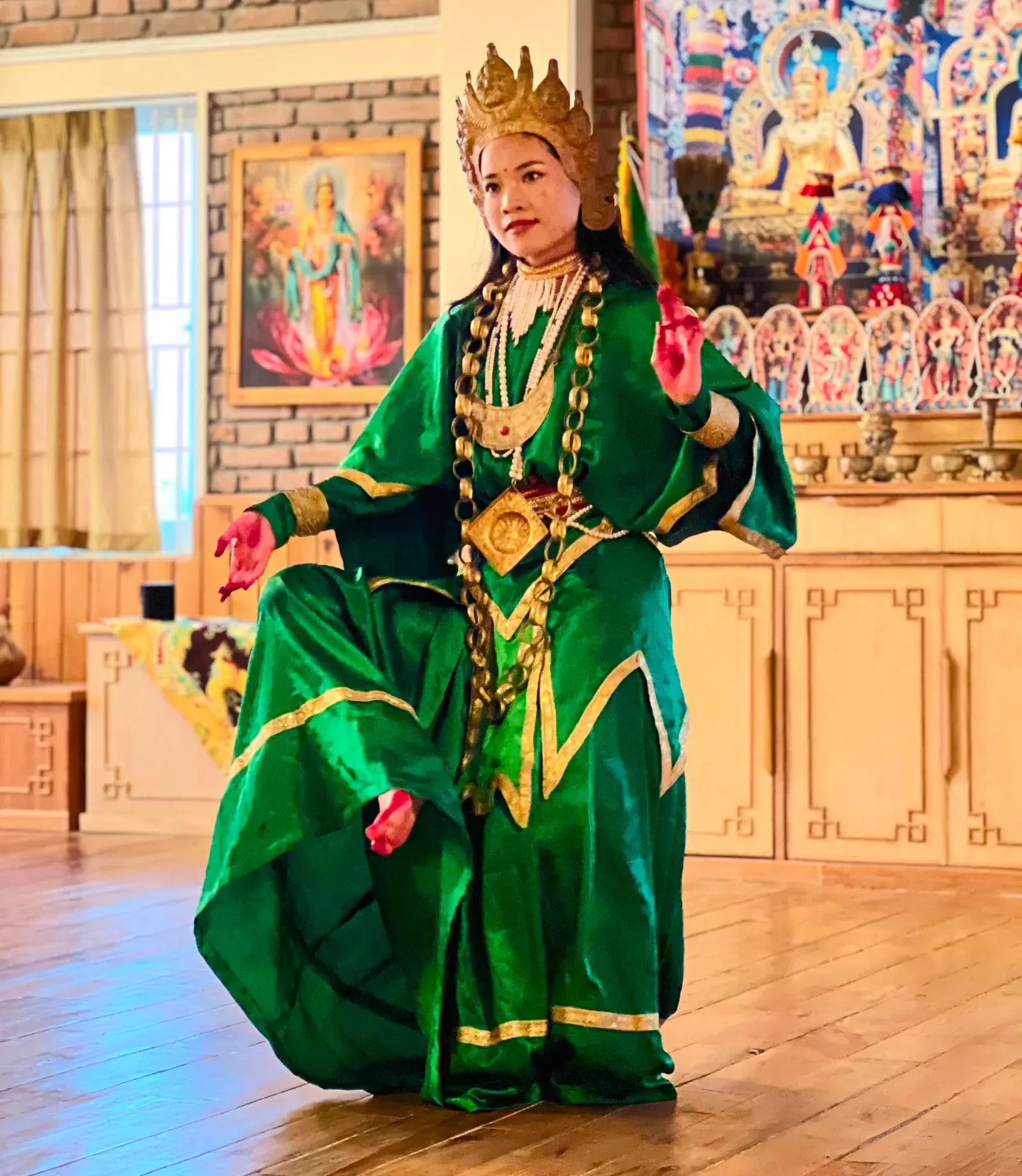 Dancer in a green Tara costume and golden crown performing in the shrine hall